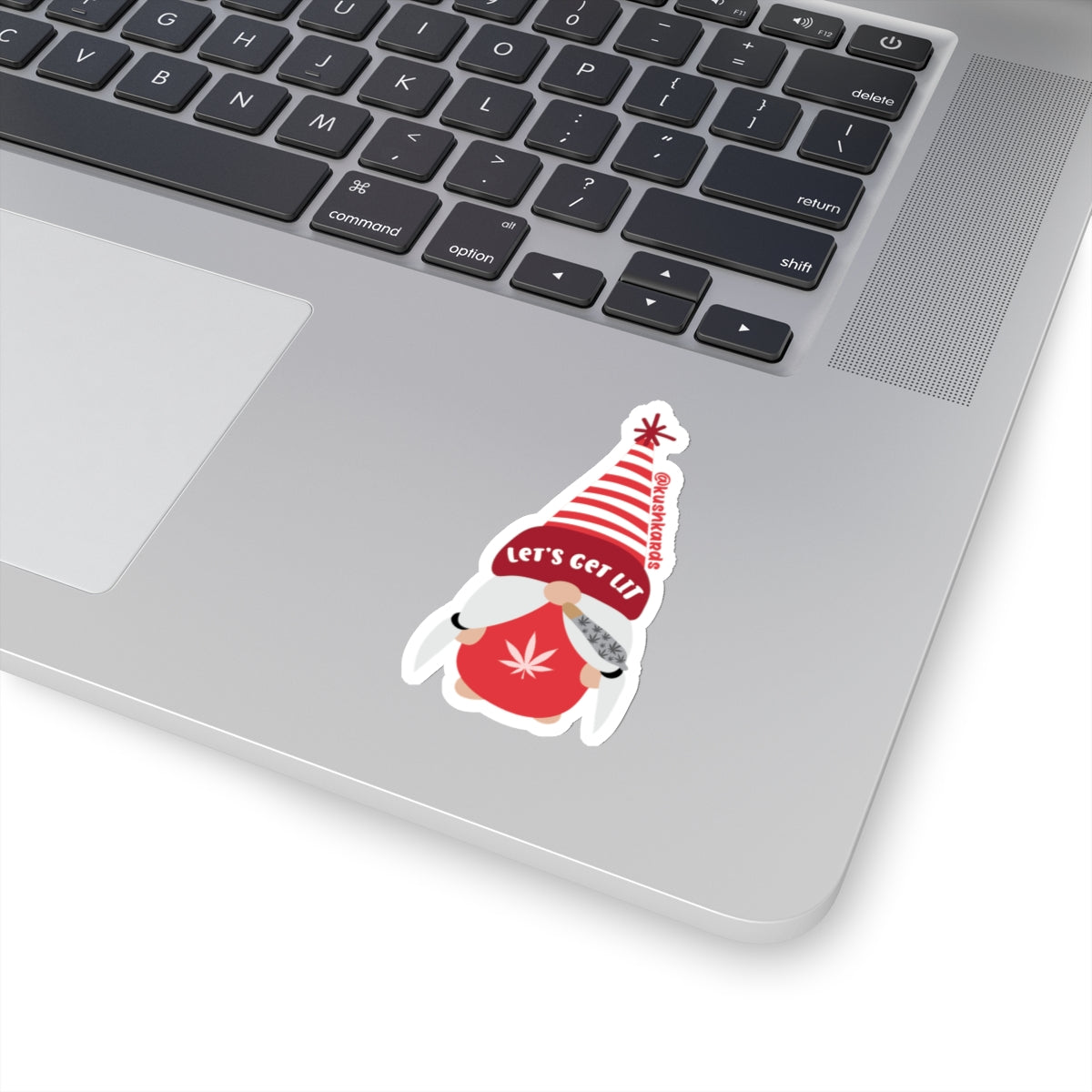 A festive gnome wearing a tall red and white striped hat with the phrase "Let’s Get Lit" written on it. The gnome has a red outfit with a cannabis leaf symbol on the chest and holds a rolled joint with cannabis leaf designs.