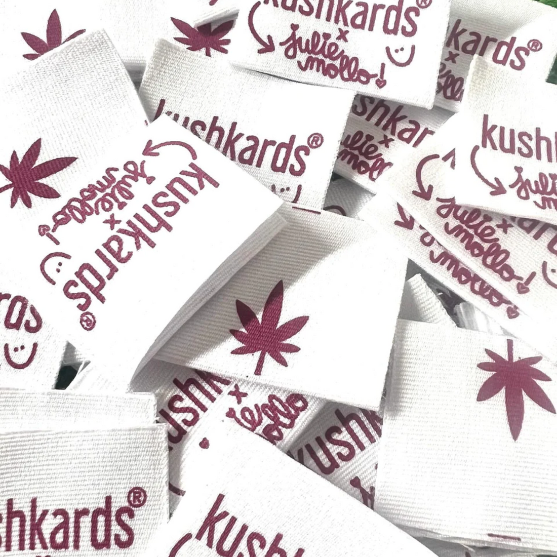 Pile of white KushKards x Julie Mollo collaboration tags with a cannabis leaf and logo.