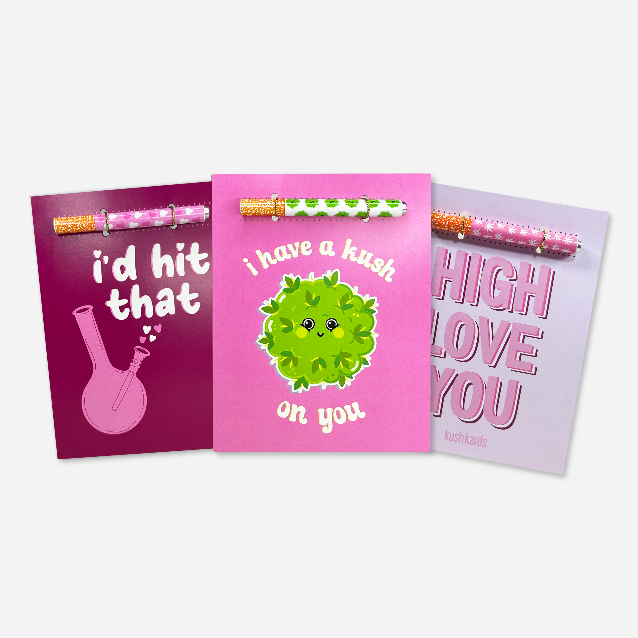 Valentine’s cannabis greeting card assortment featuring three KushKards designs with matching aluminum one-hitter pipes attached, including “I’d Hit That,” “I Have a Kush on You,” and “High Love You.”