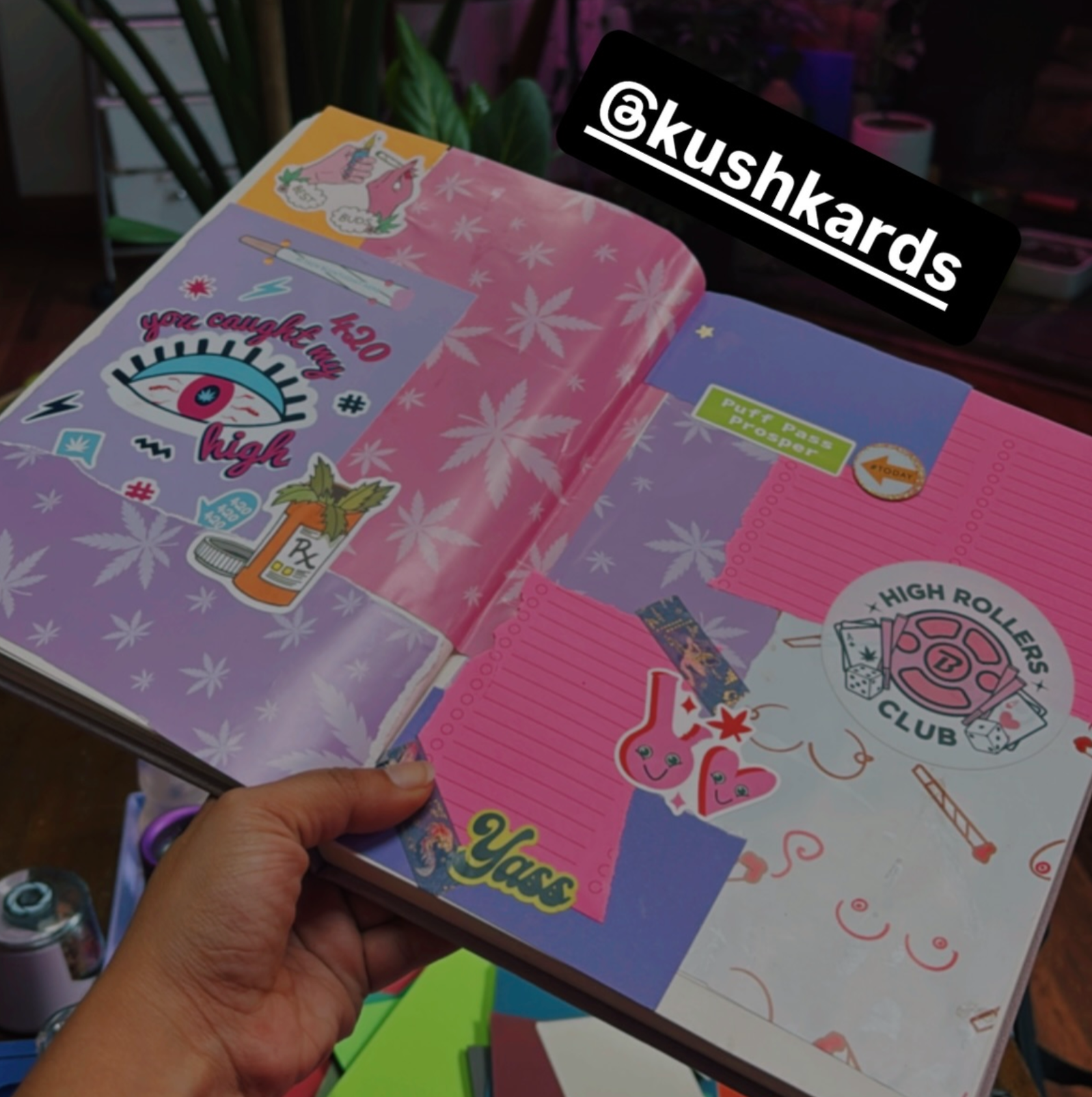 Open notebook with colorful stickers and a hand holding it, branded with &