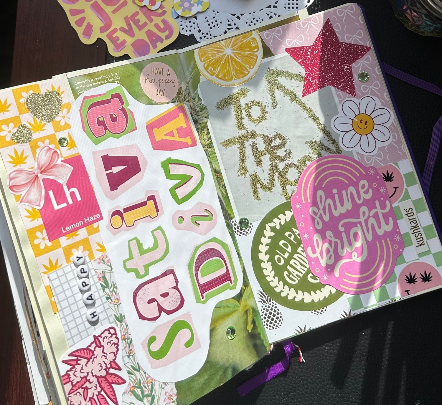 A vibrant, open junk journal spread featuring Sativa Diva stickers, including the main 'Sativa Diva' text, a cannabis leaf, a lemon, a pink glitter star, and various patterned papers. Includes text 'To The Moon' and 'Shine Bright'."