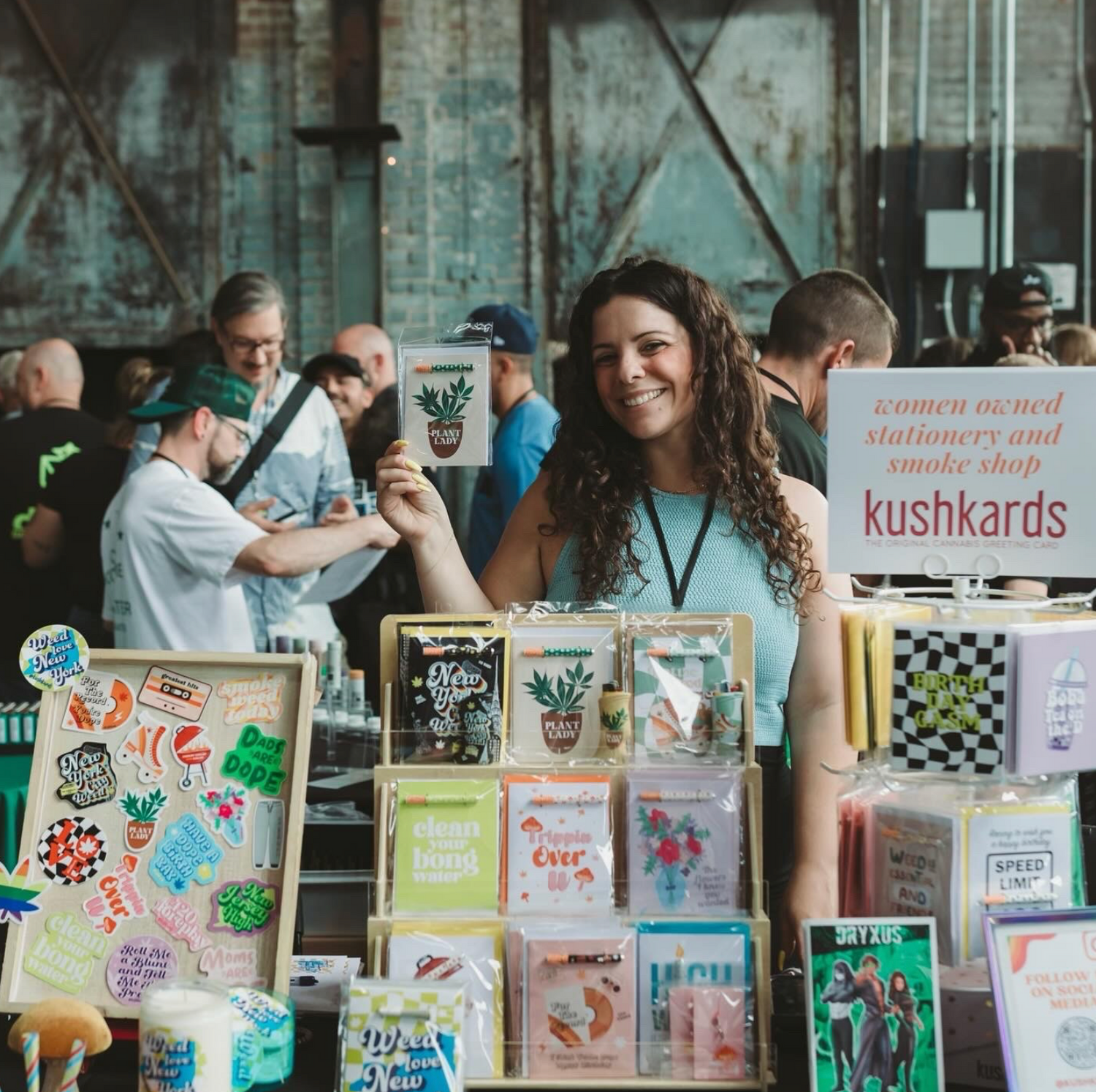 Owner of KushKards Lauren Miele standing behind tradeshow table holding a kushkard