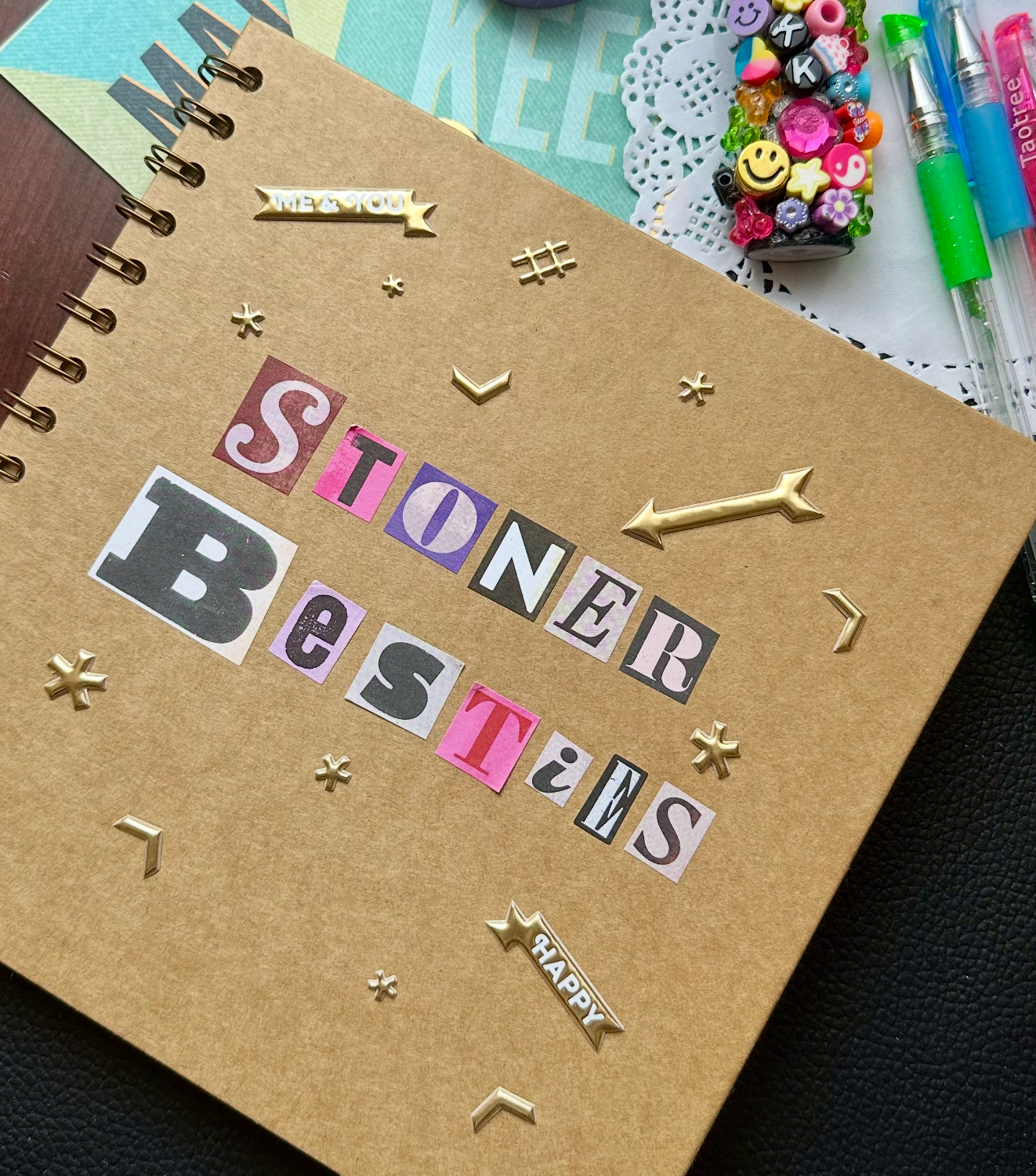 A close-up of a scrapbook cover with the words 'STONER Besties' spelled out in colorful cut-out magazine letters and adorned with gold arrow and star embellishments."