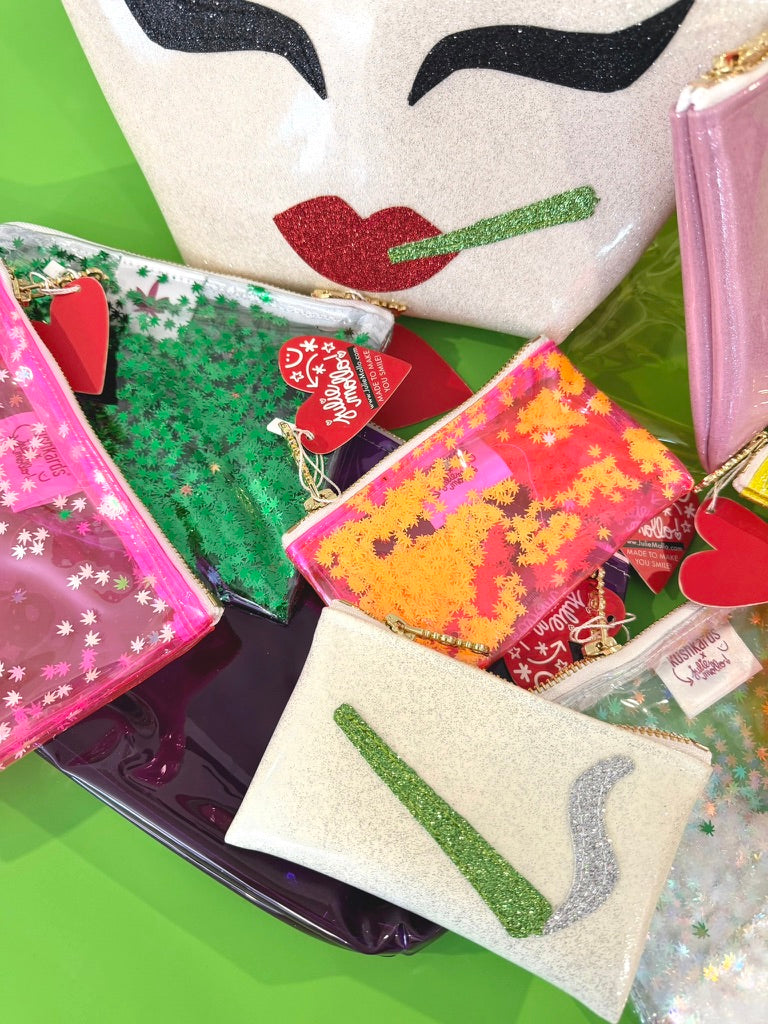 A collection of colorful glittery zippered pouches and clutch bags arranged on a bright green surface. 