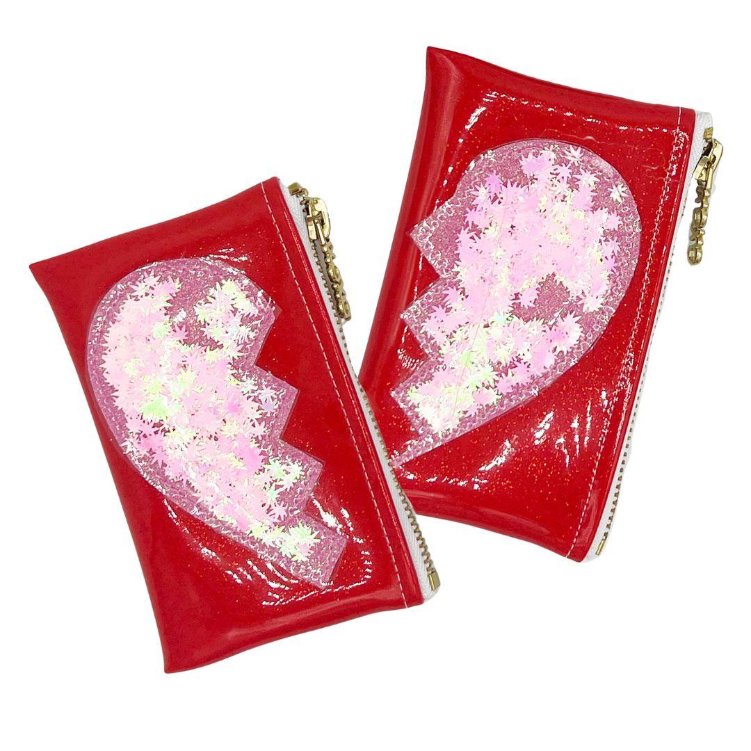Two part glitter infused Best Buds Kush Klutch set in red with pink glitter broken heart design and cannabis leaf confetti, clear vinyl overlay and gold zippers, designed by Julie Mollo