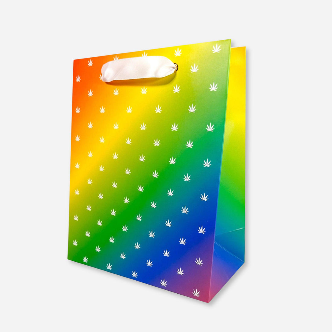 Rainbow gift bag with white cannabis leaf pattern and white ribbon handles.
