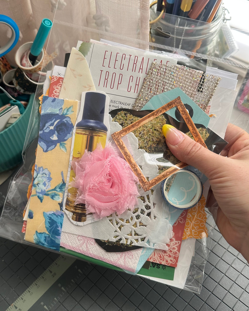 Hand holding a collage of various decorative elements on a table with crafting supplies.