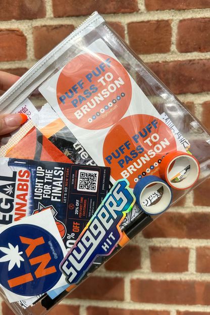 Collection of stickers in a clear plastic clutch bag against a brick wall.