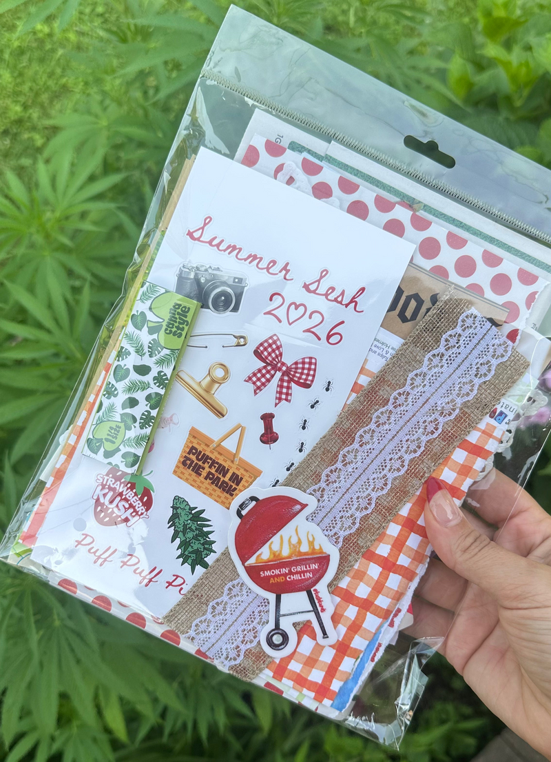 A hand holds a clear plastic bag containing a coordinated set of summer-themed stationery or craft supplies, including patterned paper, lace strips, stickers, and a white card reading 'Summer Lesh 2026,' against a background of green foliage.