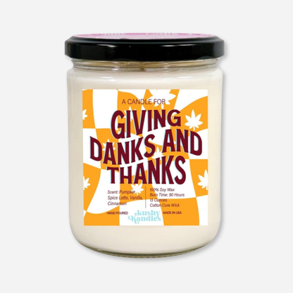 A clean product shot of the Giving Danks &amp; Thanks soy wax candle in a glass jar with a black lid. The label highlights pumpkin spice, vanilla, and cinnamon scent with a 90-hour burn time and 100% soy wax formula.