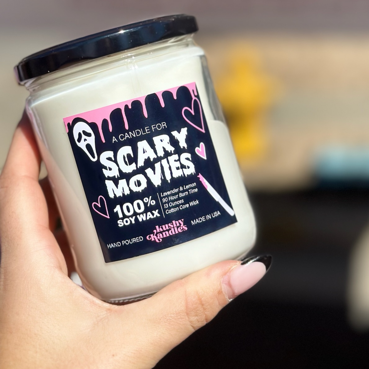 Close-up of a Scary Movies soy wax candle held outdoors, with the candle label featuring lavender and lemon scent and Ghost Face Character.