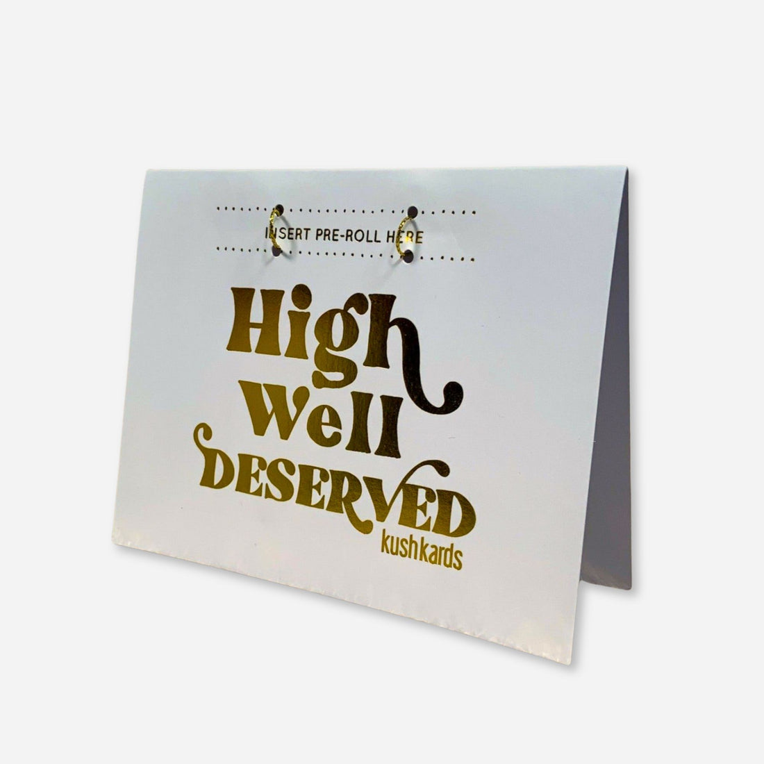 “Greeting card with the phrase ‘High Well Deserved’ in shiny gold foil lettering. A blank slot is attached above the text for inserting a pre-roll. The card is standing upright on a white background with a minimalist, elegant design.”
