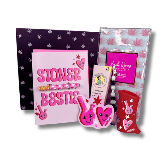 Stoner Bestie themed Valentine's Day gift box with greeting card, sticker, roach clip, lighter case, pink cones, and decorative tissue paper, all encased in a pot leaf print gift box.