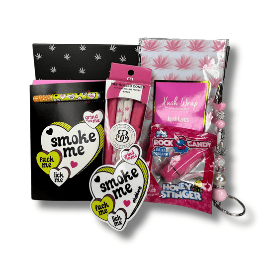 Valentine's Day Smoke Me gift box set with one hitter card, sticker, pink roach clip, cotton candy pre-roll cones, and rock candy vibrator, all in a pink and black box with decorative tissue.