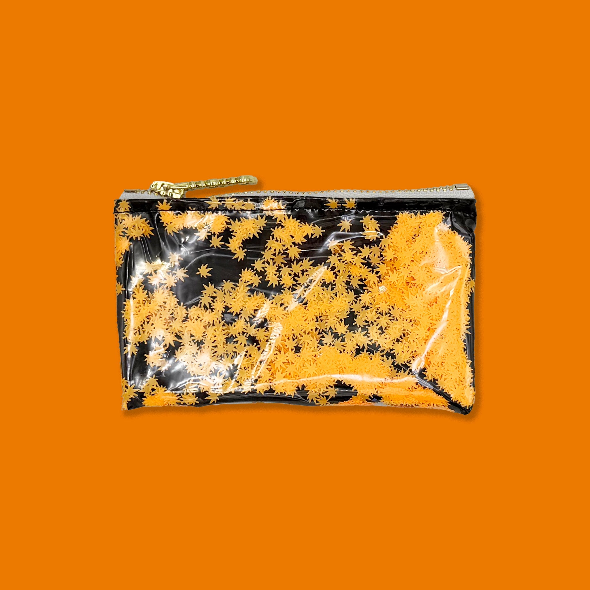 A small rectangular zip pouch with a glossy finish, featuring a black and orange pot leaf pattern, with a gold zipper and chain pull, shown on a plain orange background.
