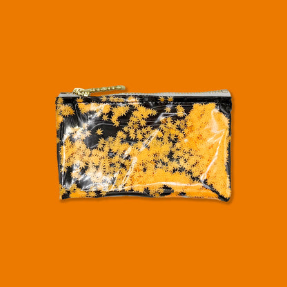 A small rectangular zip pouch with a glossy finish, featuring a black and orange pot leaf pattern, with a gold zipper and chain pull, shown on a plain orange background.