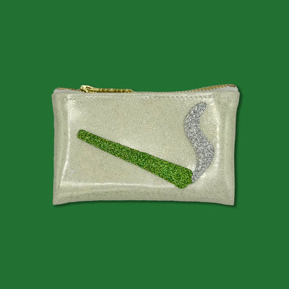 A rectangular glittery pouch in a pale champagne color with a gold zipper, featuring a green glitter rolled joint and a silver glitter smoke motif on the front, set against a solid green background.